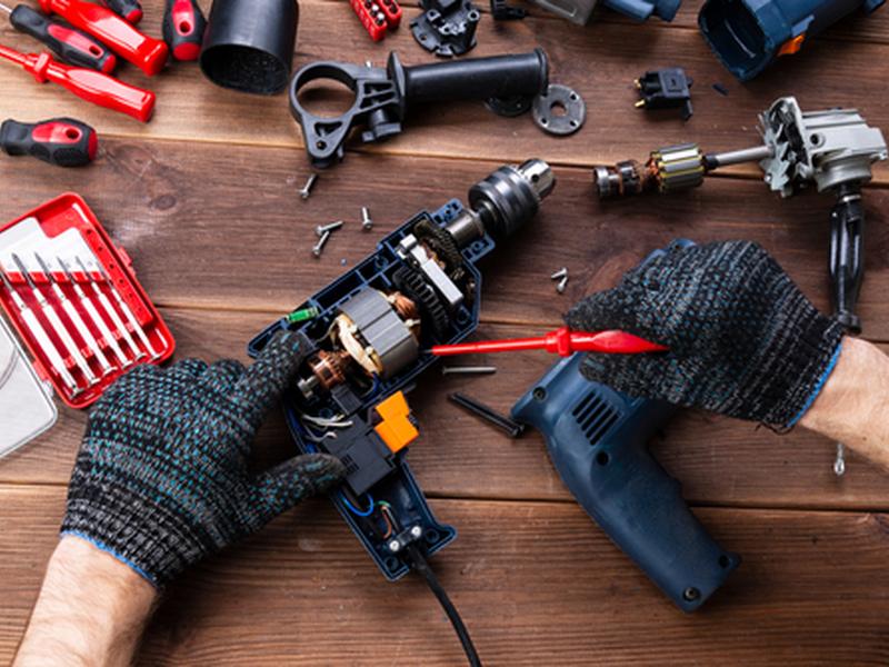 Technician repairing a disassembled power drill motor on a workbench